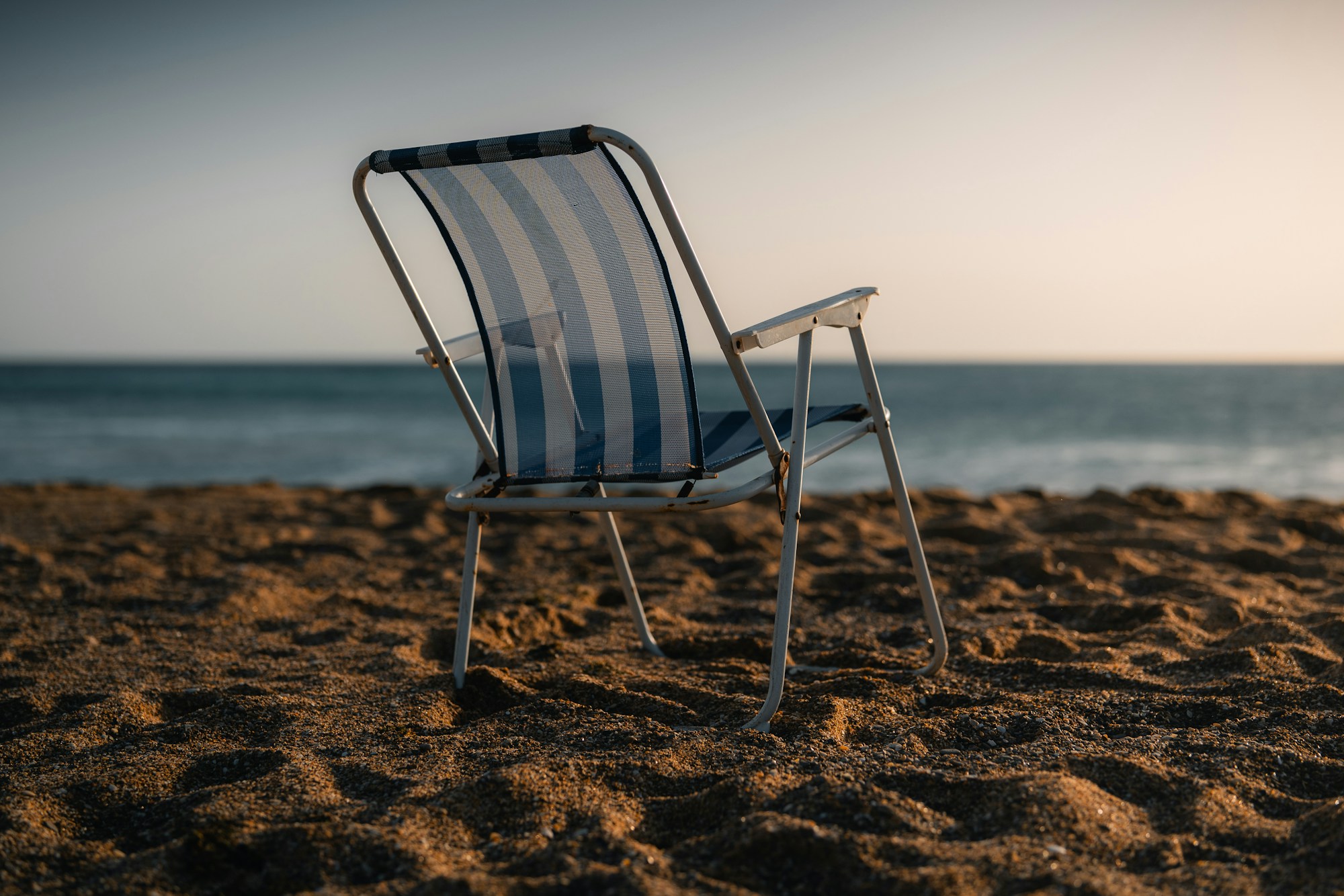 Empty striped folding beach chair facing the sea in evening light